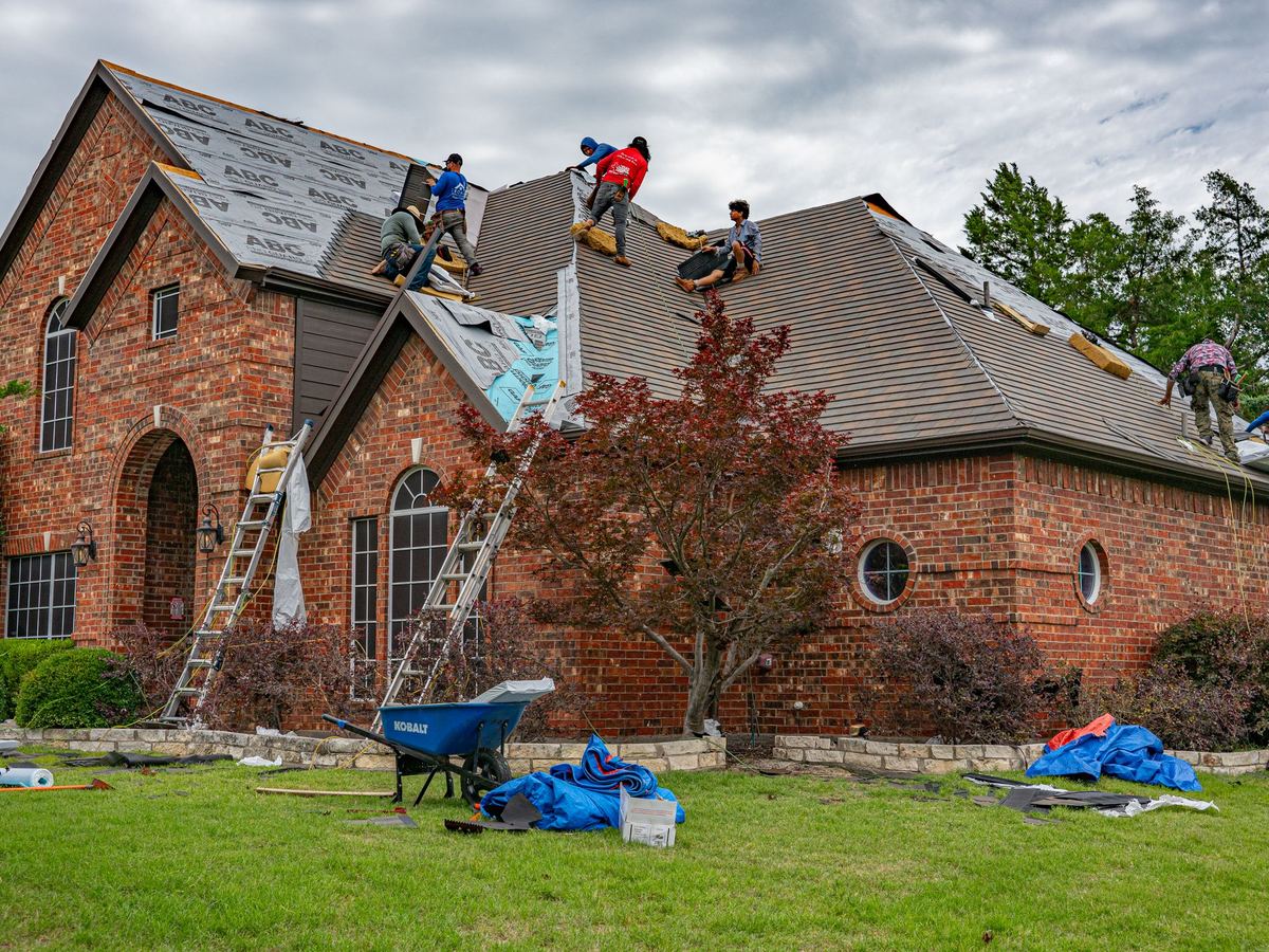 Two roofers working along the ridge of a brick house on a bright afternoon