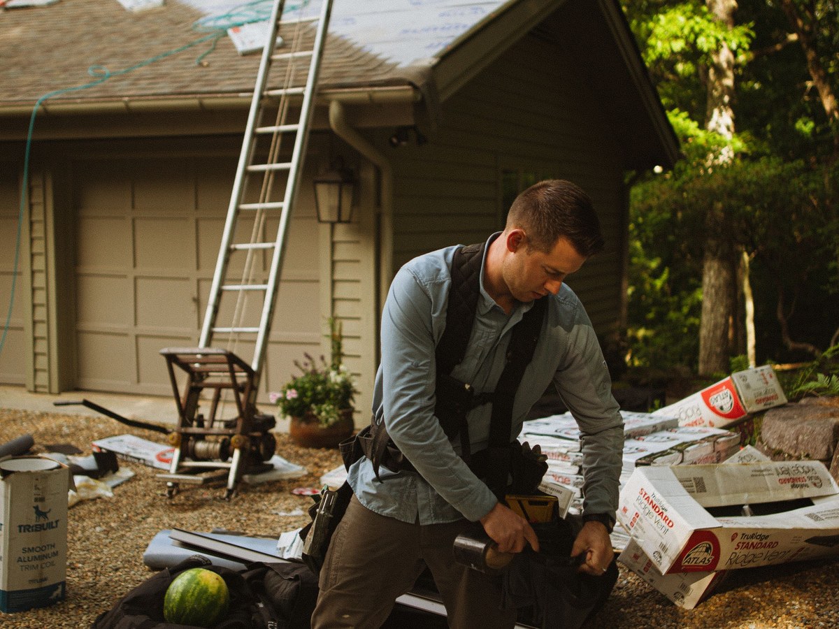 A roofing crew staging bundles of shingles beside a ladder at a house