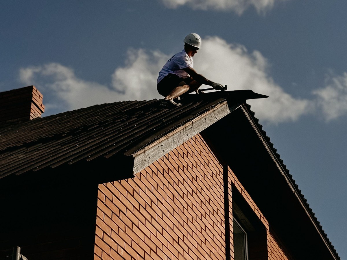 A roofer working along the ridge of a house against an open sky