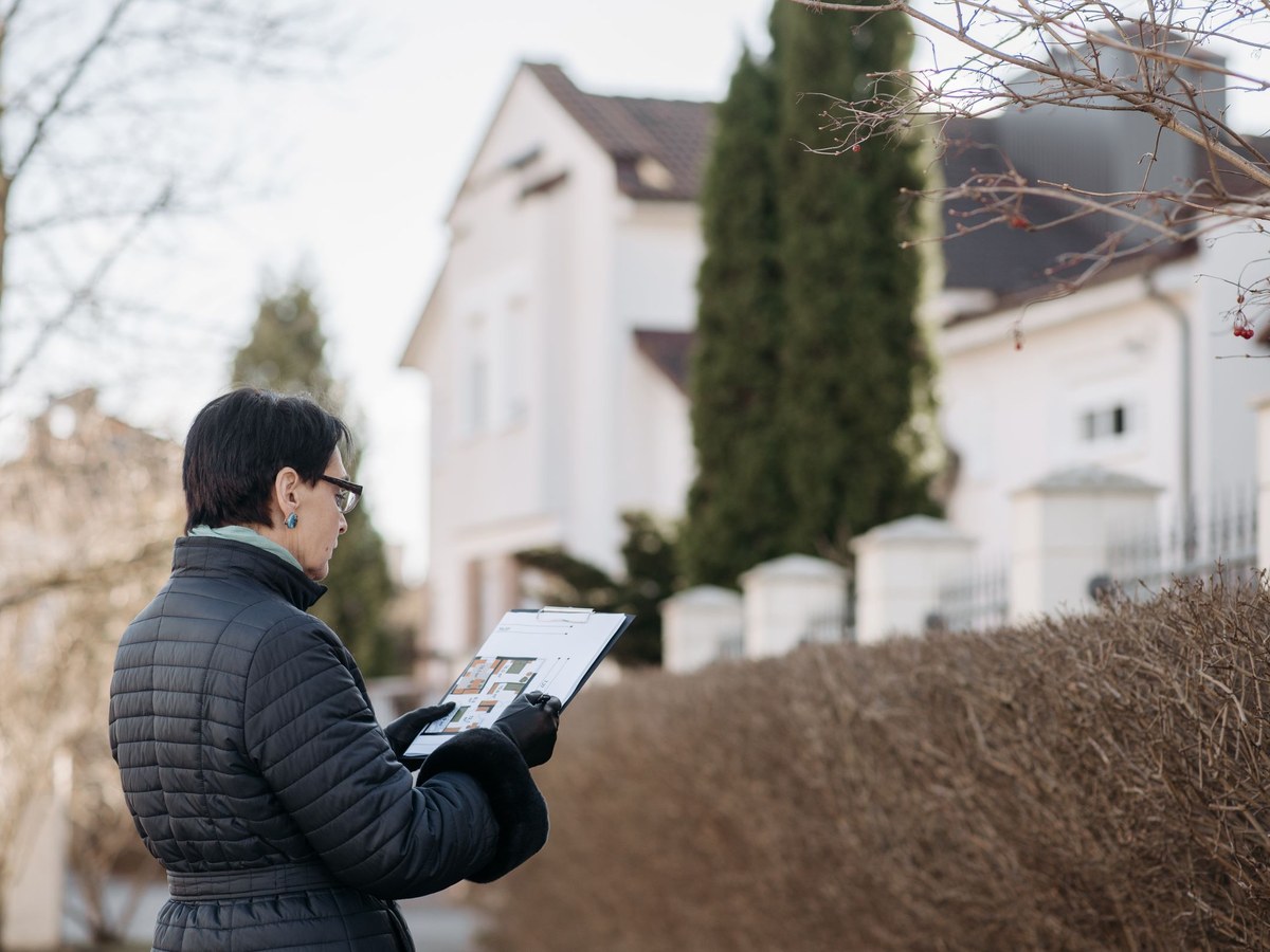 An inspector noting a roof's condition on a clipboard outside a house