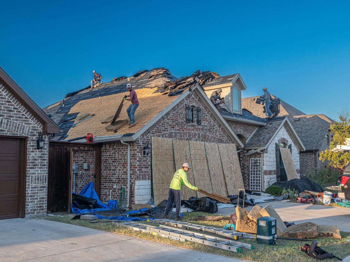Roofers working across the back slope of a brick house