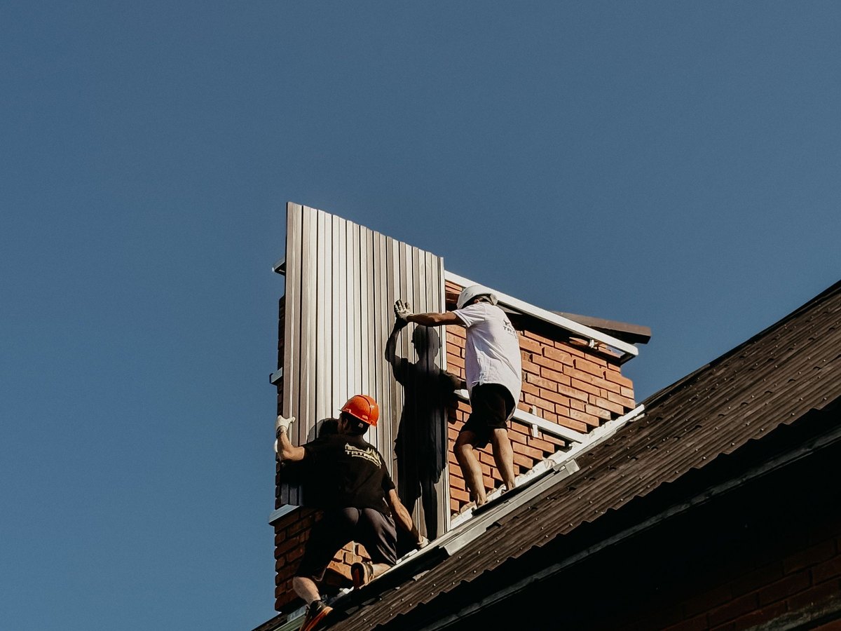 Standing seam metal roof panels going on over a brick wall